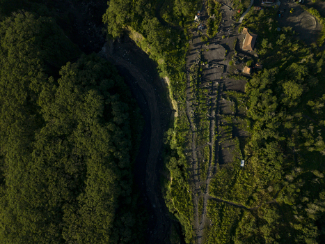 Aerial view of Bunker Kaliadem Merapi area featuring a dark volcanic riverbed surrounded by lush green forest and small structures in Kecamatan Pakem Daerah Istimewa Yogya Indonesia. Aerial view of Bunker Kaliadem Merapi area featuring a dark volcanic riverbed surrounded by lush green forest and small structures in Kecamatan Pakem Daerah Istimewa Yogya Indonesia.