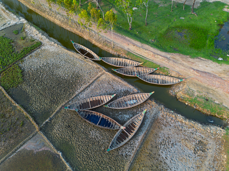 Aerial view of traditional wooden boats moored in a narrow canal beside salt pans and green fields in Moheskhali Upazila Chittagong Division Bangladesh. Aerial view of traditional wooden boats moored in a narrow canal beside salt pans and green fields in Moheskhali Upazila Chittagong Division Bangladesh.