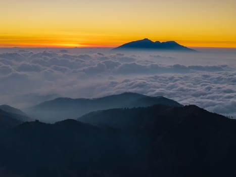 Aerial view of Mount Bromo and surrounding volcanic peaks rising above a dense sea of clouds during a vibrant golden sunset in Tosari East Java Indonesia. Aerial view of Mount Bromo and surrounding volcanic peaks rising above a dense sea of clouds during a vibrant golden sunset in Tosari East Java Indonesia.