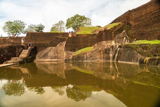 View of the ancient water tank and stone ruins of Sigiriya Rock Fortress with tourists walking on stairs and reflections on the water Sigiriya Central Province Sri Lanka. View of the ancient water tank and stone ruins of Sigiriya Rock Fortress with tourists walking on stairs and reflections on the water Sigiriya Central Province Sri Lanka.
