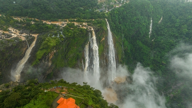 Aerial view of Jog Falls cascading down lush green cliffs with mist and dense forest in Kargal Karnataka India.