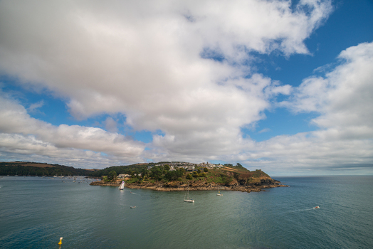 View of the Fowey River estuary with sailing boats the town of Fowey nestled on the hillside and lush coastal landscape under a blue sky in Fowey Cornwall United Kingdom. View of the Fowey River estuary with sailing boats the town of Fowey nestled on the hillside and lush coastal landscape under a blue sky in Fowey Cornwall United Kingdom.