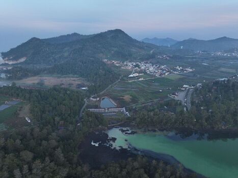 Aerial view of the Dieng Plateau landscape featuring a green lake volcanic hills agricultural fields and a village Kejajar Central Java Indonesia. Aerial view of the Dieng Plateau landscape featuring a green lake volcanic hills agricultural fields and a village Kejajar Central Java Indonesia.