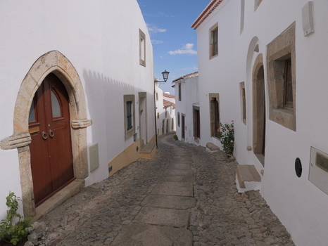 View of a narrow cobblestone street lined with traditional white washed buildings and stone door frames in Marvao Portalegre District Portugal. View of a narrow cobblestone street lined with traditional white washed buildings and stone door frames in Marvao Portalegre District Portugal.
