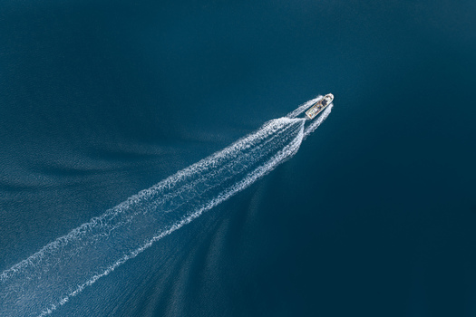 Aerial view of a small white boat cruising across deep blue sea water leaving a long white foamy wake in Itoshima Fukuoka Japan. Aerial view of a small white boat cruising across deep blue sea water leaving a long white foamy wake in Itoshima Fukuoka Japan.