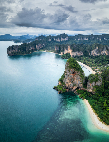 Aerial view of Railay Beach featuring dramatic limestone cliffs turquoise waters and sandy coastline under a cloudy sky in Ao Nang Krabi Thailand. Aerial view of Railay Beach featuring dramatic limestone cliffs turquoise waters and sandy coastline under a cloudy sky in Ao Nang Krabi Thailand.