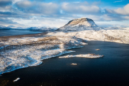 Aerial view of the snow covered Saana mountain rising above the dark waters of Lake Kilpisjarvi in the Arctic landscape of Kilpisjarvi Lapland Finland. Aerial view of the snow covered Saana mountain rising above the dark waters of Lake Kilpisjarvi in the Arctic landscape of Kilpisjarvi Lapland Finland.