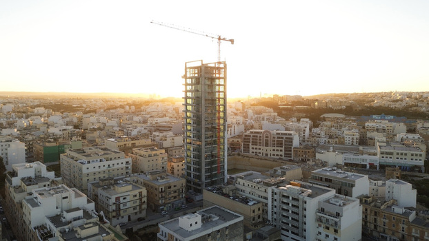 Aerial view of a modern high rise building under construction with a crane on top surrounded by dense urban architecture in Valletta Port Region Malta. Aerial view of a modern high rise building under construction with a crane on top surrounded by dense urban architecture in Valletta Port Region Malta.