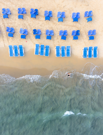 Aerial view of Bat Yam beach with blue sunbeds and chairs on the golden sand near turquoise water with a person swimming in the waves Bat Yam Center District Israel. Aerial view of Bat Yam beach with blue sunbeds and chairs on the golden sand near turquoise water with a person swimming in the waves Bat Yam Center District Israel.