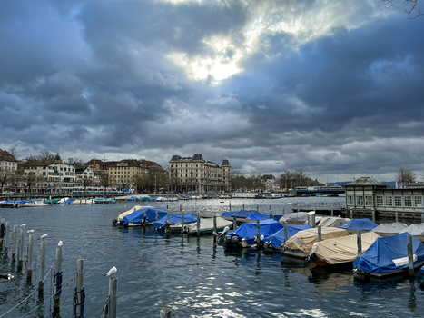 View of boats docked at the harbor with covered vessels historic buildings in the background and a dramatic cloudy sky over Zurich Zurich Switzerland.