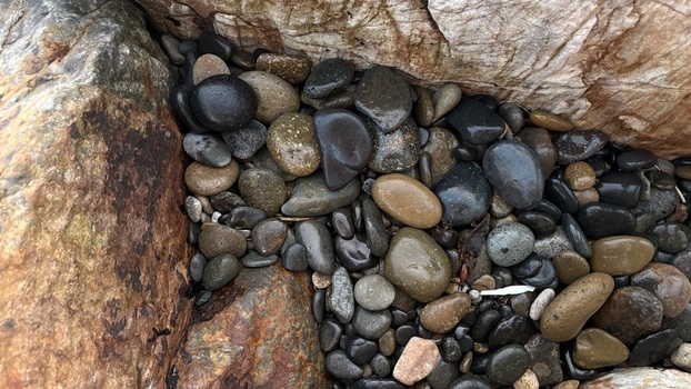 View of smooth wet pebbles and river stones nestled between large textured rocks Oceanside California United States. View of smooth wet pebbles and river stones nestled between large textured rocks Oceanside California United States.