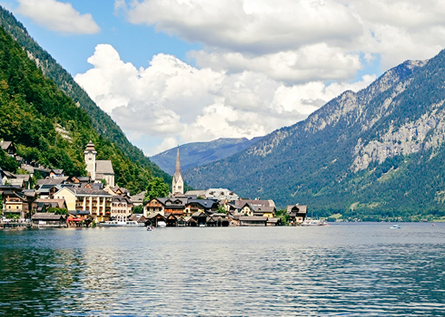 View of the historic village of Hallstatt with its traditional alpine architecture church spire and surrounding mountains reflected in the calm lake water in Hallstatt Upper Austria Austria. View of the historic village of Hallstatt with its traditional alpine architecture church spire and surrounding mountains reflected in the calm lake water in Hallstatt Upper Austria Austria.