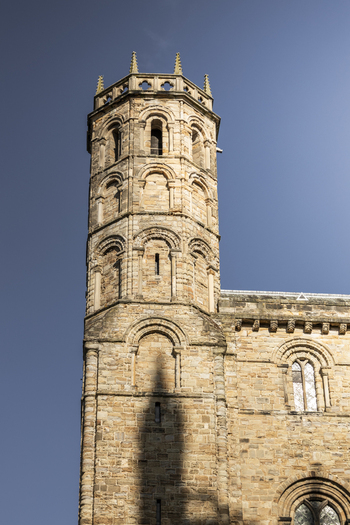 View of the historic stone tower of Durham Cathedral with arched windows and intricate masonry against a clear blue sky in Durham England United Kingdom. View of the historic stone tower of Durham Cathedral with arched windows and intricate masonry against a clear blue sky in Durham England United Kingdom.