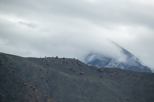 View of rugged mountain slopes under a heavy blanket of clouds and mist with snow capped peaks in the distance Chilas Gilgit Pakistan. View of rugged mountain slopes under a heavy blanket of clouds and mist with snow capped peaks in the distance Chilas Gilgit Pakistan.