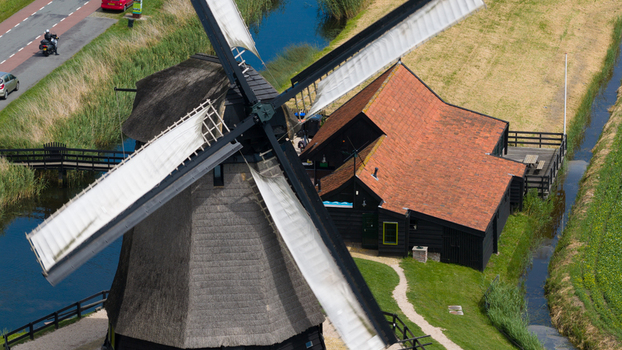 Aerial view of the historic Schermerhorn windmill with its traditional thatched roof and wooden structure situated beside a canal and green fields in Schermerhorn North Holland Netherlands. Aerial view of the historic Schermerhorn windmill with its traditional thatched roof and wooden structure situated beside a canal and green fields in Schermerhorn North Holland Netherlands.