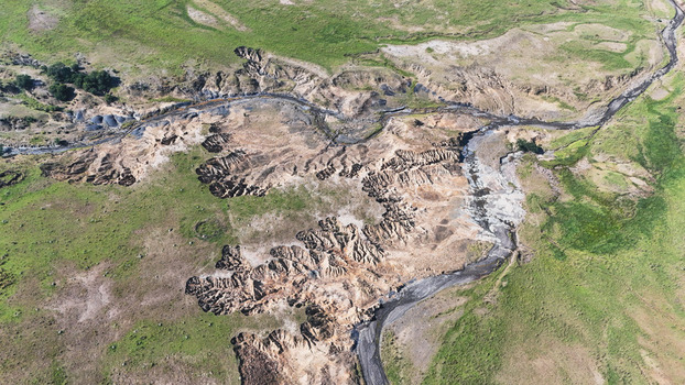Aerial view of severe soil erosion and deep dongas cutting through green grassy fields along a dry riverbed in Pietermaritzburg KwaZulu Natal South Africa.