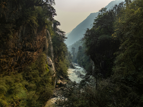 Aerial view of a river flowing through a deep forested gorge with steep rocky cliffs and lush vegetation in Nepal.