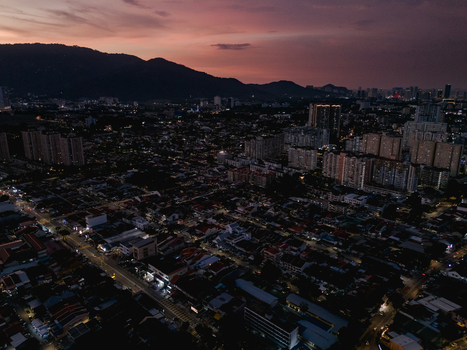 Aerial view of George Town at twilight featuring illuminated city streets dense residential buildings and distant mountains under a dusky purple sky in George Town Penang Malaysia. Aerial view of George Town at twilight featuring illuminated city streets dense residential buildings and distant mountains under a dusky purple sky in George Town Penang Malaysia.