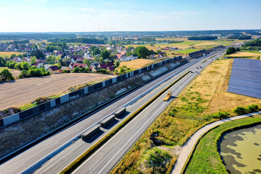 Aerial view of a highway with noise barriers passing trucks and a solar farm next to a rural village under a clear sky Hochstadt Bavaria Germany. Aerial view of a highway with noise barriers passing trucks and a solar farm next to a rural village under a clear sky Hochstadt Bavaria Germany.