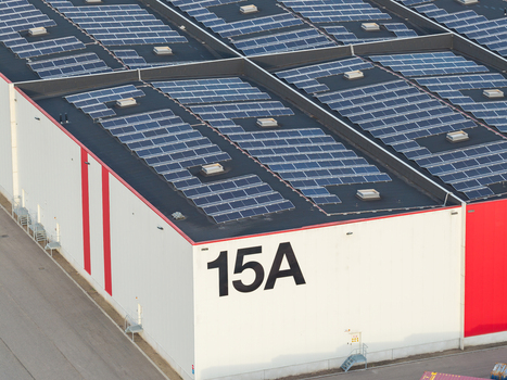 Aerial view of a large industrial warehouse roof covered with extensive solar panel arrays featuring the number 15A on the side wall in Genk Flanders Belgium. Aerial view of a large industrial warehouse roof covered with extensive solar panel arrays featuring the number 15A on the side wall in Genk Flanders Belgium.