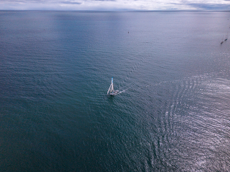 Aerial view of a lone sailboat navigating the deep blue waters off the coast of Fowey Cornwall United Kingdom. Aerial view of a lone sailboat navigating the deep blue waters off the coast of Fowey Cornwall United Kingdom.