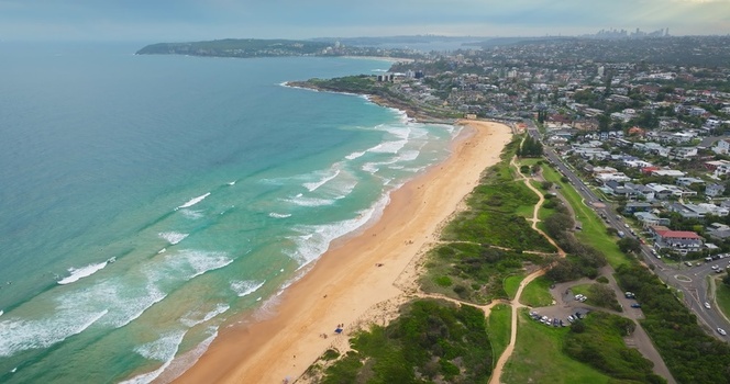 Aerial view of the coastline with turquoise waves crashing onto the sandy beach bordered by green parkland and residential houses in Sydney New South Wales Australia. Aerial view of the coastline with turquoise waves crashing onto the sandy beach bordered by green parkland and residential houses in Sydney New South Wales Australia.