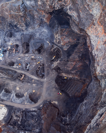 Aerial view of an open pit mine with heavy machinery excavated dark soil and winding access roads in Iceland. Aerial view of an open pit mine with heavy machinery excavated dark soil and winding access roads in Iceland.