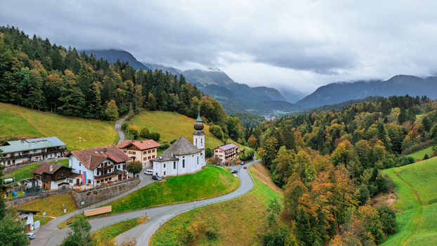 Aerial view of the Maria Gern church nestled in the alpine landscape with autumn foliage winding roads and mountains in the background in Berchtesgaden Bavaria Germany.
