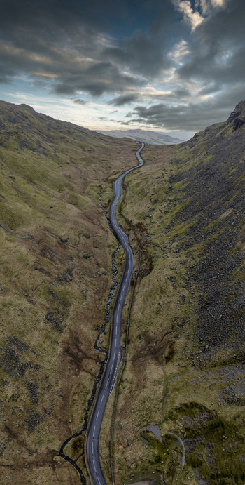 Aerial view of a road snaking through the dramatic valley cutting through the rugged landscape under a moody sky revealing the raw beauty of the region City Name England United Kingdom. Aerial view of a road snaking through the dramatic valley cutting through the rugged landscape under a moody sky revealing the raw beauty of the region City Name England United Kingdom.