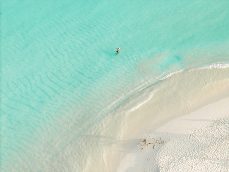 Aerial view of a solitary figure wading through the serene turquoise waters meeting the pristine white sands of Kan island Dhidhdhoo Maldives.