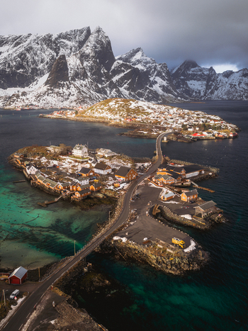 Aerial view of small islands connected by bridges rugged peaks dusted with snow reflecting in the tranquil turquoise waters Sakris&oslash;ya Norway.