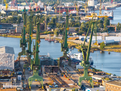 Aerial view of the industrial shipyard in Gdansk featuring large green cranes ship hulls under construction and industrial infrastructure along the waterfront in Pomeranian Voivodeship Poland. Aerial view of the industrial shipyard in Gdansk featuring large green cranes ship hulls under construction and industrial infrastructure along the waterfront in Pomeranian Voivodeship Poland.