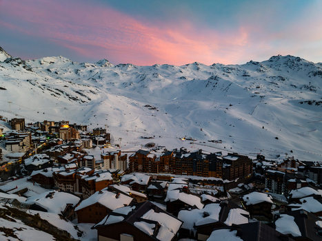 Aerial view of chalets nestled amidst snow covered slopes with the sky ablaze in hues of pink and orange Val Thorens Auvergne Rh&ocirc;ne Alpes France.