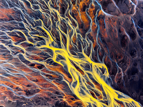 Aerial view of a vibrant braided river system featuring striking yellow and blue glacial sediment patterns flowing through dark volcanic terrain Iceland. Aerial view of a vibrant braided river system featuring striking yellow and blue glacial sediment patterns flowing through dark volcanic terrain Iceland.