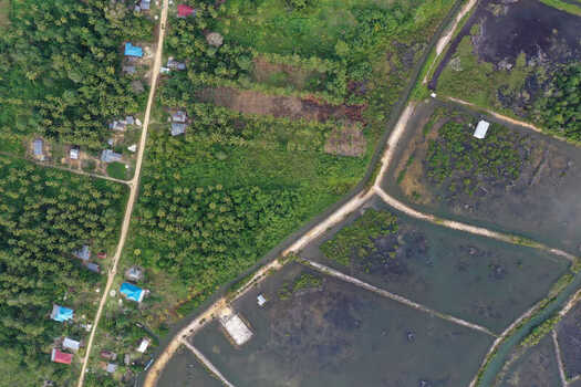 Aerial view of rural landscape featuring small houses with blue roofs palm trees and aquaculture ponds in Maginti South East Sulawesi Indonesia. Aerial view of rural landscape featuring small houses with blue roofs palm trees and aquaculture ponds in Maginti South East Sulawesi Indonesia.