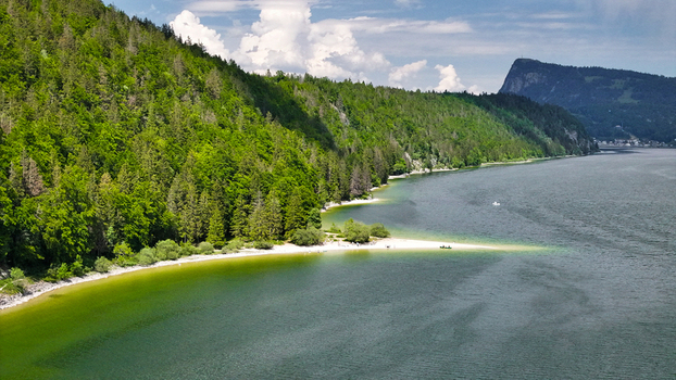 Aerial view of the turquoise waters meet the emerald forests surrounding Lac de Joux revealing a serene sandbar Le Lieu Vaud Switzerland.