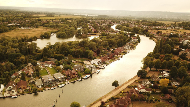 Aerial view of Thames River winding through a residential area with lush trees houses along the banks and small boats moored in the water Thames United Kingdom. Aerial view of Thames River winding through a residential area with lush trees houses along the banks and small boats moored in the water Thames United Kingdom.