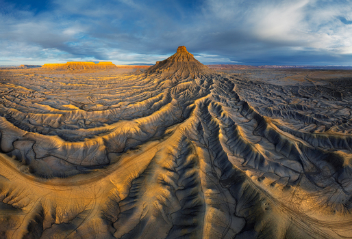 Aerial view of the Factory Butte badlands featuring intricate eroded ridges golden sunlight and deep shadows in the desert landscape of Hanksville Utah United States.