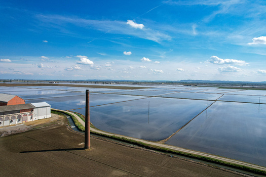 Aerial view of Azienda Agricola Veneria with flooded rice fields a tall brick chimney and farm buildings under a blue sky in Veneria Piemonte Italy. Aerial view of Azienda Agricola Veneria with flooded rice fields a tall brick chimney and farm buildings under a blue sky in Veneria Piemonte Italy.