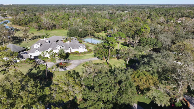 Aerial view of a large residential estate featuring a tennis court manicured lawns and mature trees in a suburban setting in Plant City Florida United States.