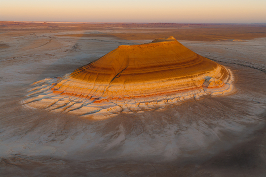 Aerial view of a majestic layered butte with golden geological strata and eroded white base in the desert landscape of Mangystau Region Kazakhstan. Aerial view of a majestic layered butte with golden geological strata and eroded white base in the desert landscape of Mangystau Region Kazakhstan.