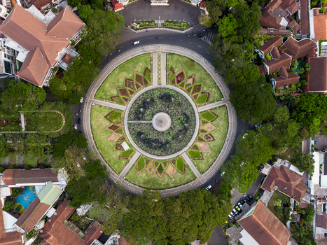 Aerial view of Alun Alun Tugu Malang a circular park featuring a central fountain and lotus pond surrounded by lush trees and historic colonial architecture in Malang East Java Indonesia.