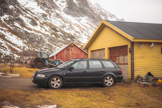 View of a black station wagon parked in front of yellow and red wooden buildings against a backdrop of snow dusted mountains Skjelfjorden Norway. View of a black station wagon parked in front of yellow and red wooden buildings against a backdrop of snow dusted mountains Skjelfjorden Norway.