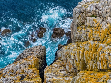 Aerial view of the rugged cliffs of Silence Beach Viewpoint with turquoise waves crashing against the yellow toned rocks Cudillero Asturias Spain.