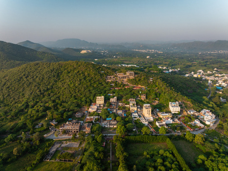 Aerial view of residential buildings nestled on a green hillside with lush vegetation and clear sky in Udaipur Rajasthan India.
