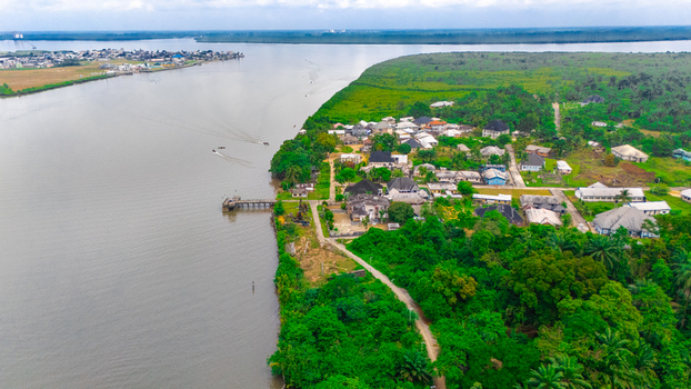 Aerial view of a riverside settlement with houses nestled among lush green trees and vegetation along the banks of a wide river in Minima Rivers Nigeria.