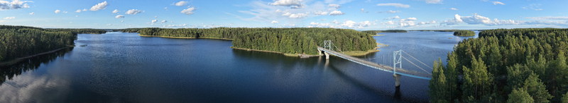 Aerial view of Potkusalmen silta Bridge spanning the calm waters of the lake surrounded by dense pine forests under a bright blue sky in Savonlinna Etela Savo Finland.
