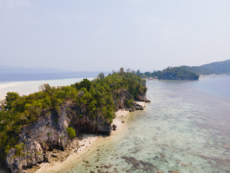 Aerial view of Ransiwor homestay on a lush tropical island with rocky cliffs white sand beaches and clear turquoise waters in Raja Ampat Southwest Papua Indonesia. Aerial view of Ransiwor homestay on a lush tropical island with rocky cliffs white sand beaches and clear turquoise waters in Raja Ampat Southwest Papua Indonesia.