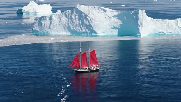Aerial view of sailboat with red sails near icebergs Greenland. Aerial view of sailboat with red sails near icebergs Greenland.