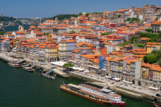 Aerial view of terracotta rooftops cascade down to the Douro River boats line the shore reflecting the vibrant buildings Porto Porto District Portugal. Aerial view of terracotta rooftops cascade down to the Douro River boats line the shore reflecting the vibrant buildings Porto Porto District Portugal.